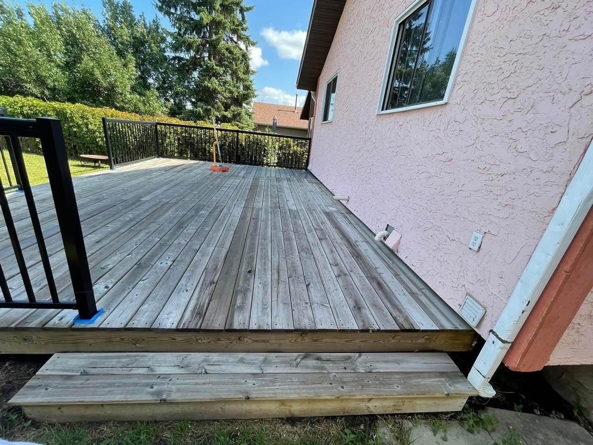 Weathered grey cedar deck boards with black aluminum railing before staining — Calgary deck refinishing by Timeless Interiors Ltd